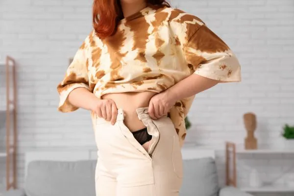Image of woman trying to do her trousers up after pregnancy weight gain City of London