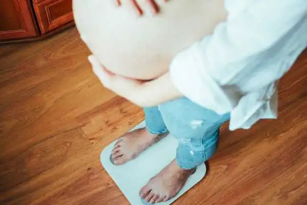 Image of woman weighing herself and experiencing weight gain through pregnancy City of London